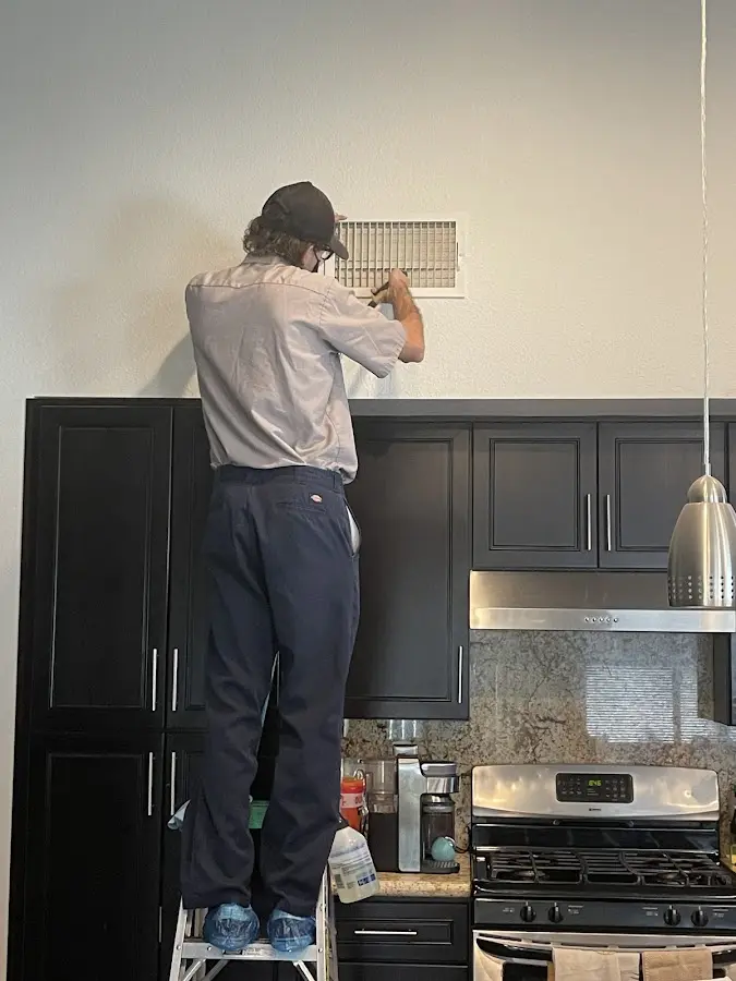 Technician inspecting an air vent during HVAC service in Vista